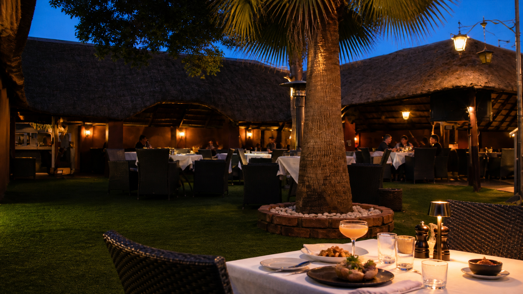 Thatched courtyard lounge at blue hour with a palm and set tables